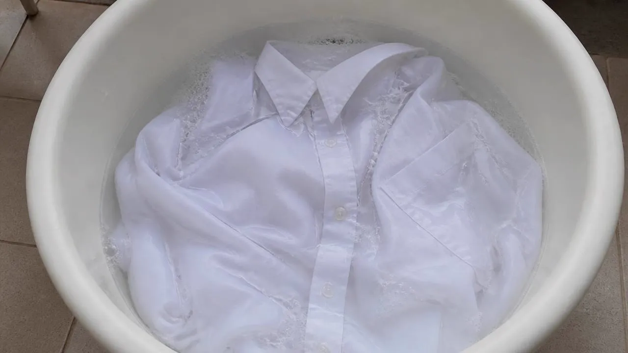 A white cotton shirt soaking in an oxygen bleach solution to lift yellow antiperspirant staining.
